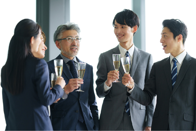 バーベキュー交流会で食事を囲みながら笑顔で談笑する社員の様子、社内表彰式で登壇者のプレゼンテーションを聞く社員の様子、懇親会で乾杯しながら和やかに交流する社員の様子、打ち上げの席でグラスを手に会話を楽しむ社員の様子